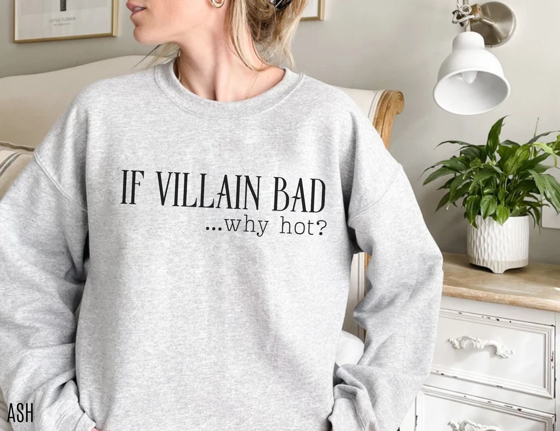 woman wearing an ash grey sweatshirt that says if villain bad why hot standing beside white nightstand