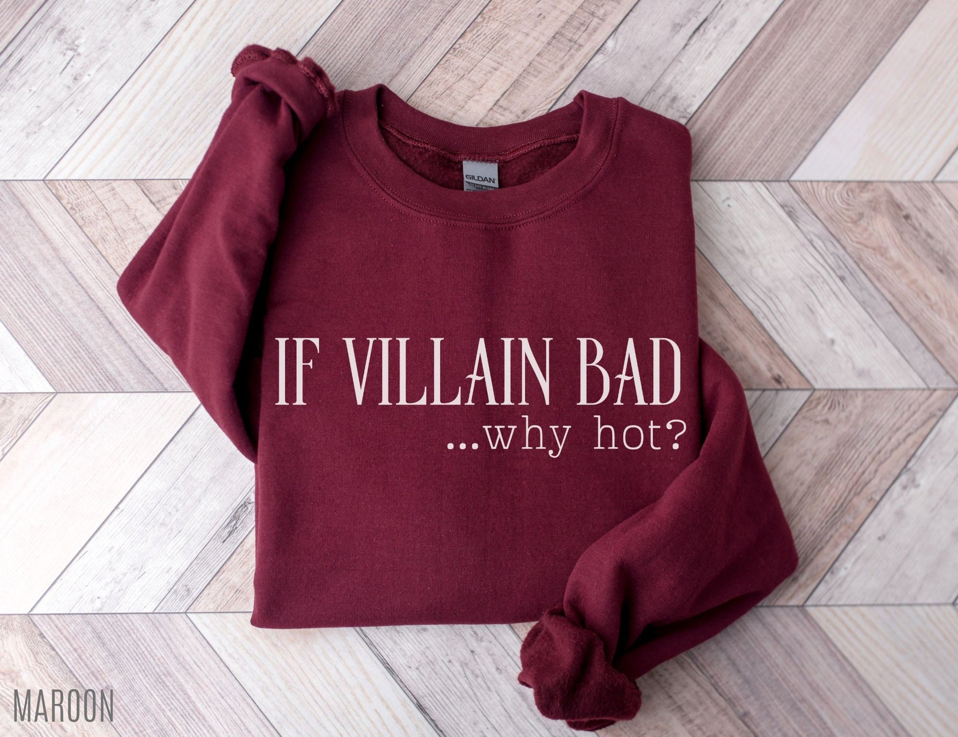 folded maroon sweatshirt that says if villain bad why hot styled on wood herringbone background