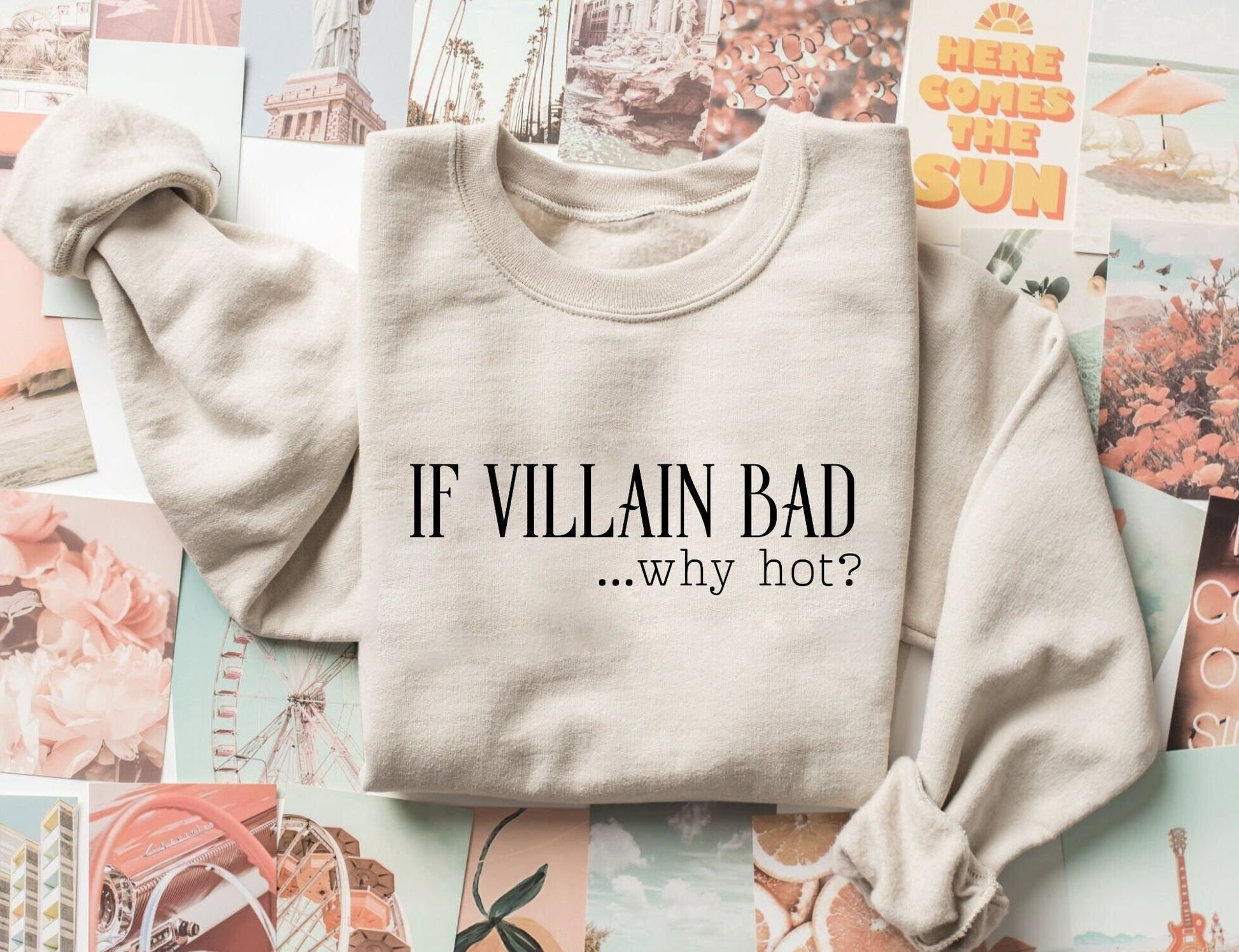 folded sand-colored sweatshirt with text if villain bad why hot on a collage of pastel and beach postcards