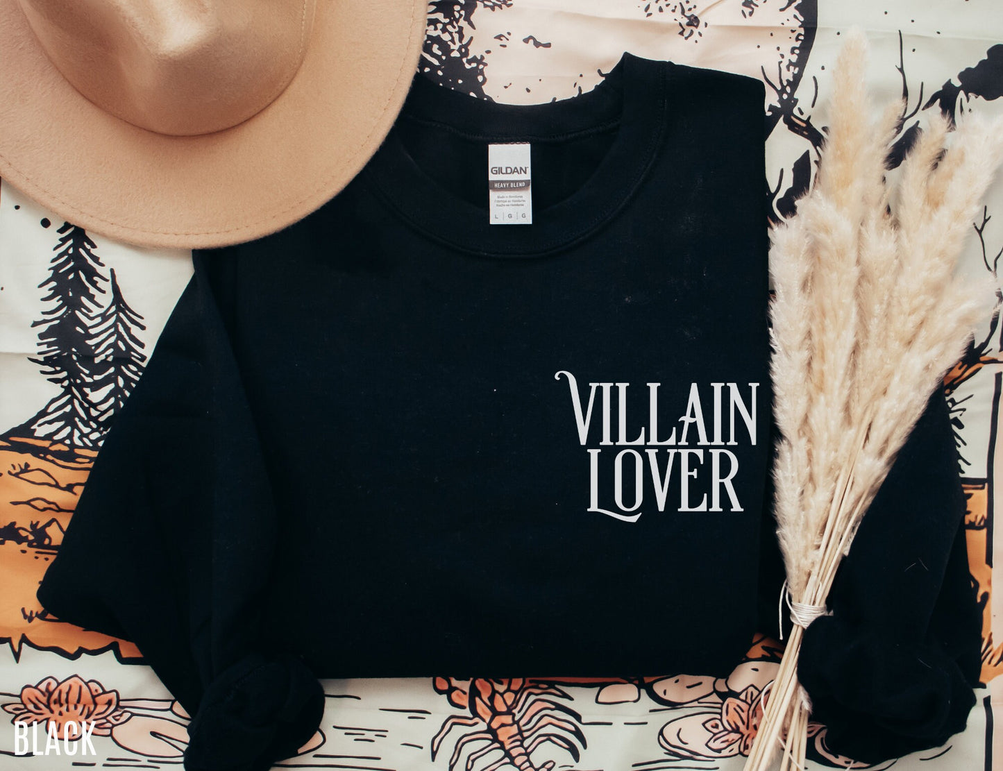 folded black sweatshirt with villain lover text styled with beige hat and boho bookish background