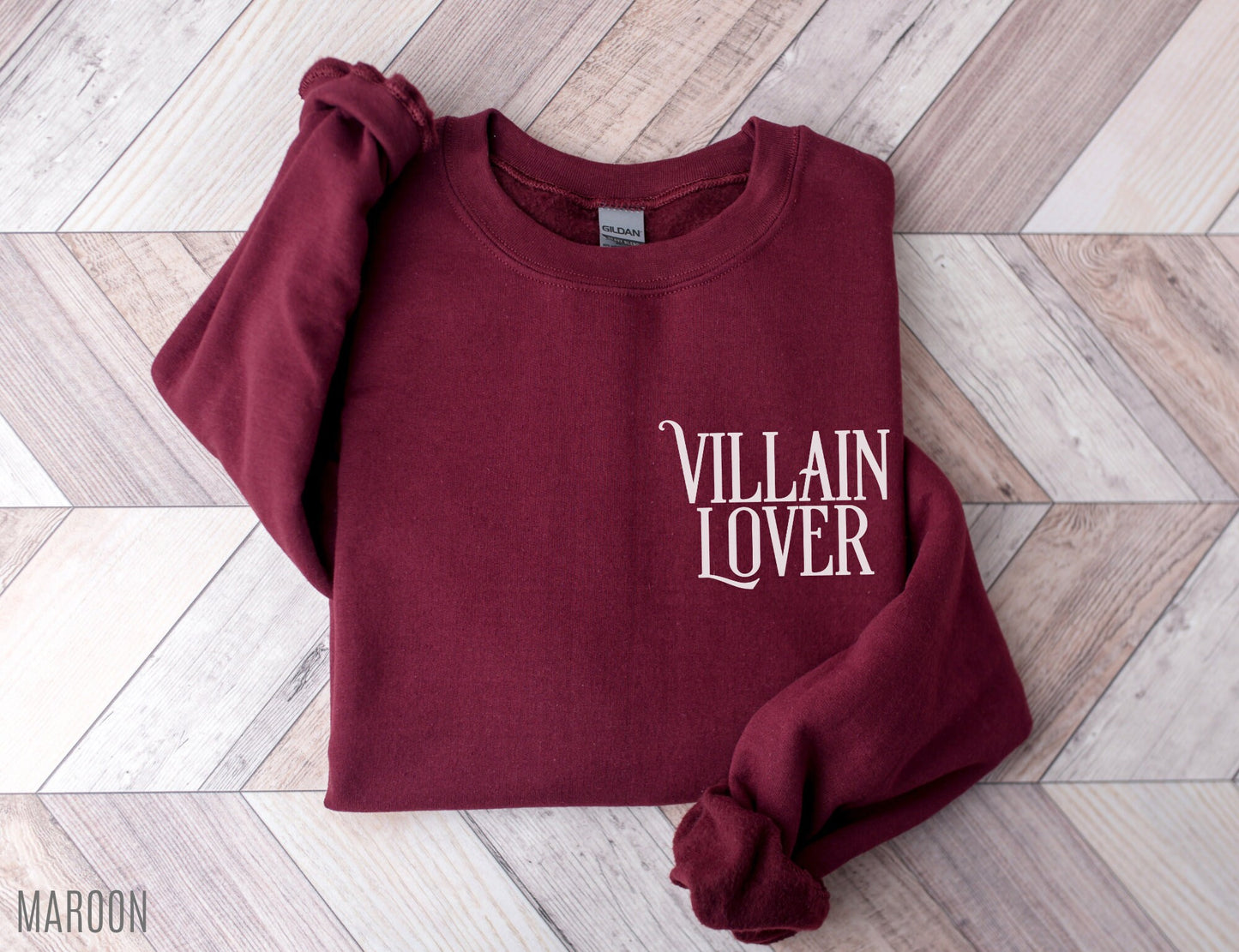 folded maroon sweatshirt with villain lover text on wood herringbone background