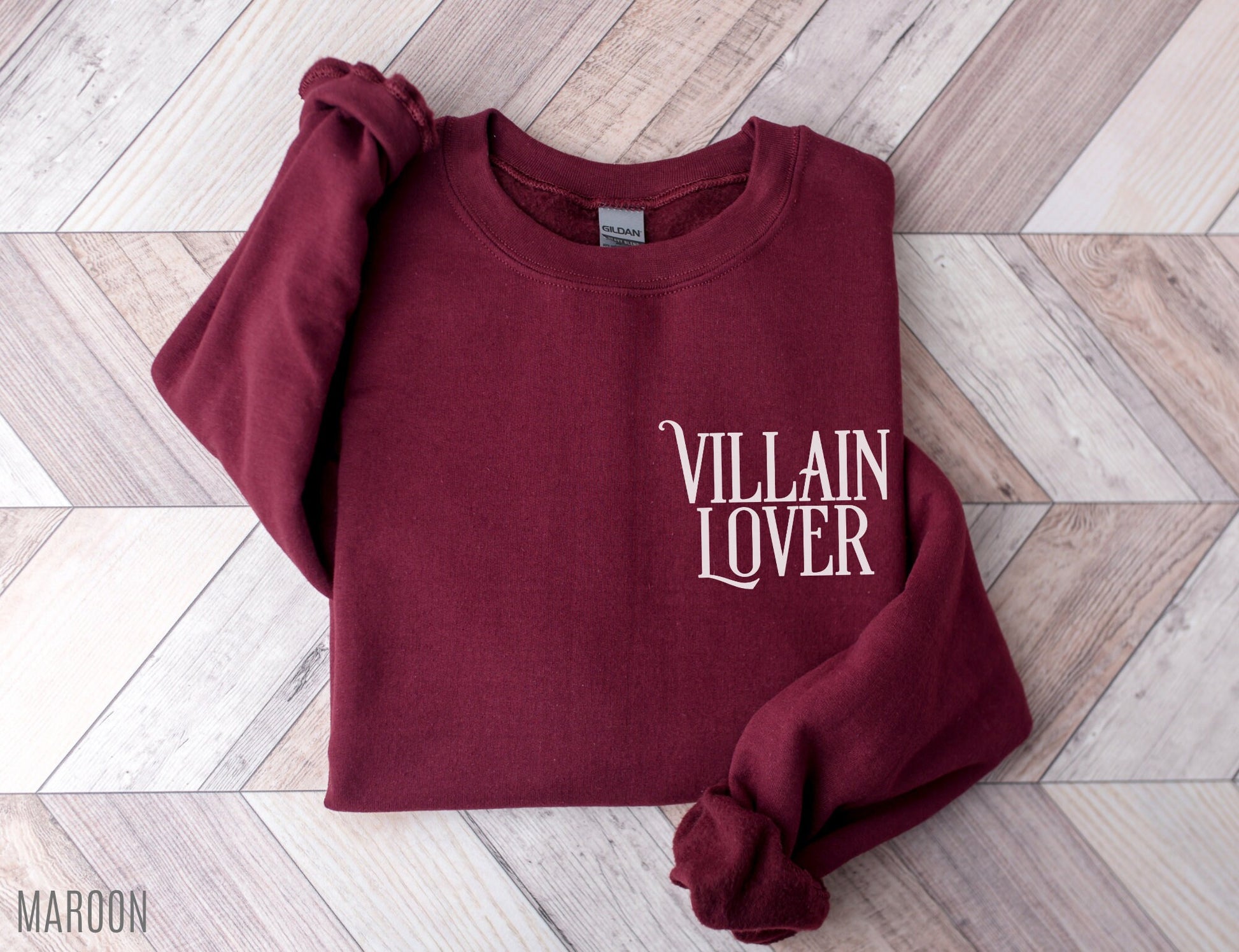 folded maroon sweatshirt with villain lover text on wood herringbone background