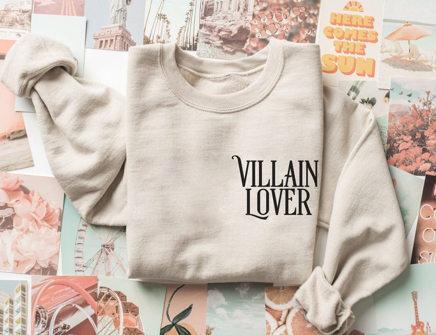 folded sand-colored sweatshirt with villain lover text on top of pastel and vintage photo collage