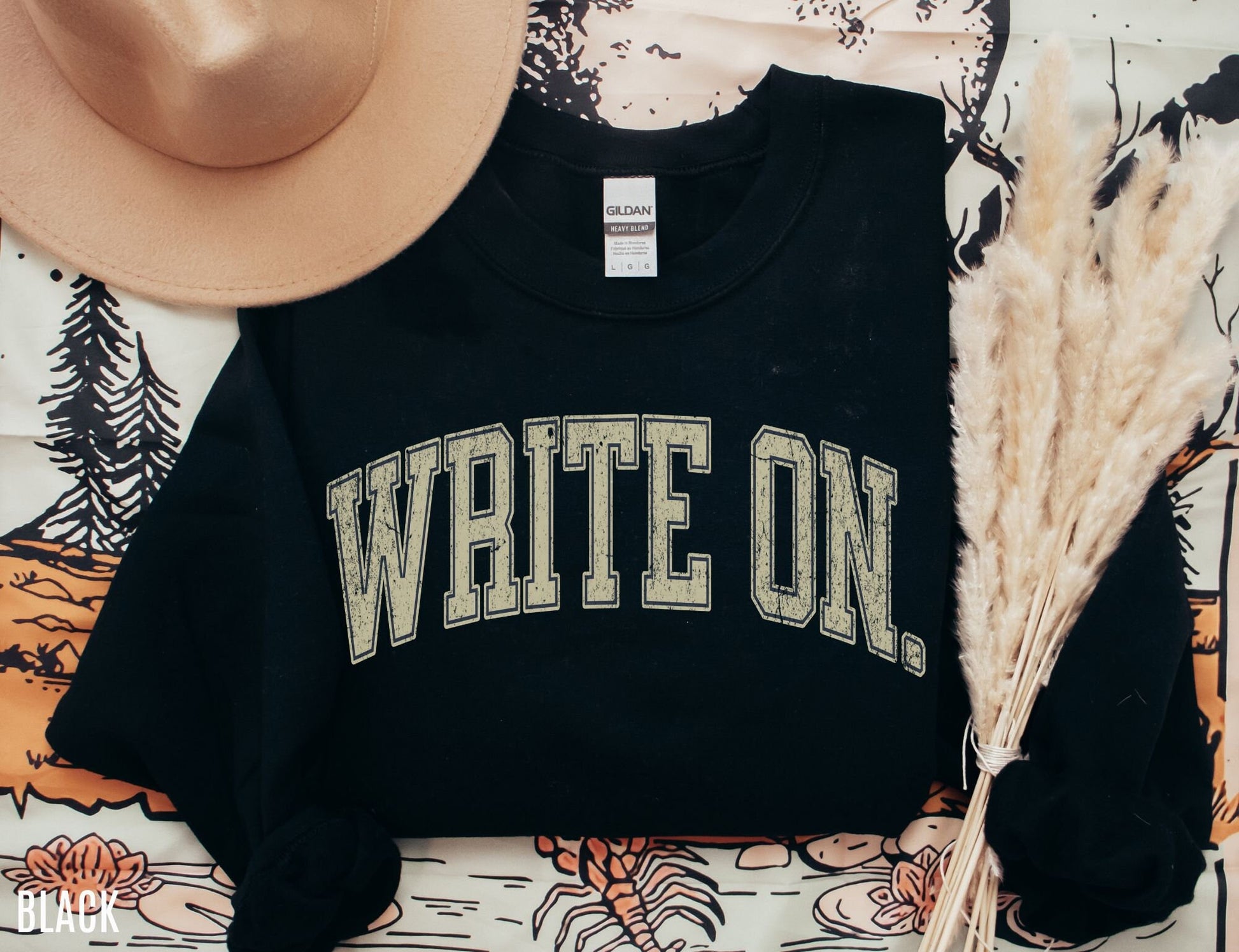 flatlay of black write on sweatshirt with rustic tan text, styled with hat and fall florals