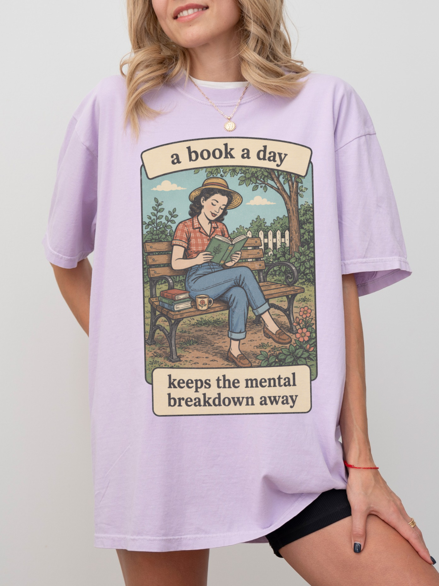 Woman wearing a orchid oversized t shirt with vintage illustration of girl reading on a bench and text a book a day keeps the mental breakdown away