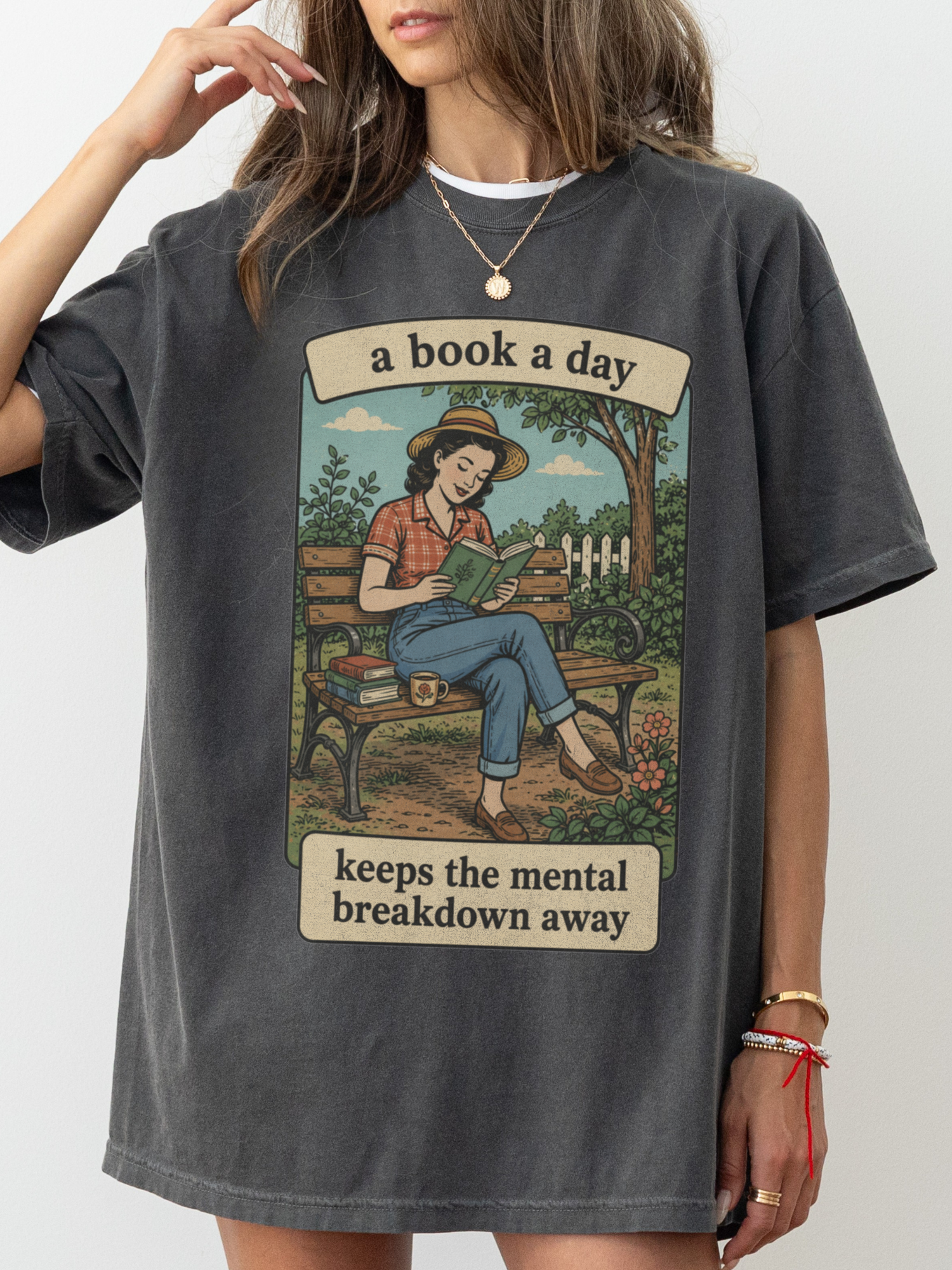 Woman wearing a pepper oversized t shirt with retro reading girl graphic sitting on bench and text a book a day keeps the mental breakdown away