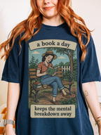 Woman wearing a true navy blue oversized t shirt with retro book lover graphic of woman reading on a park bench and text a book a day keeps the mental breakdown away