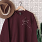 maroon sweatshirt with minimalist white star constellation and the phrase I remember you hanging next to a felt hat and cactus