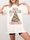 Ivory Comfort Colors shirt modeled with an All Booked for Christmas design featuring stacked red and green vintage books shaped like a Christmas tree with evergreen greenery, ornaments, berries and a gold star