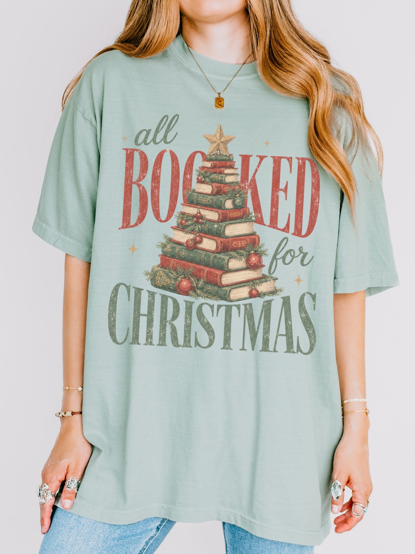 Bay Comfort Colors shirt featuring an All Booked for Christmas design with a Christmas tree made of stacked vintage books, evergreen branches, red ornaments and gold star, festive bookish Christmas shirt for readers