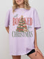Orchid Comfort Colors shirt featuring an All Booked for Christmas design with a Christmas tree of stacked red and green books decorated with evergreen branches, ornaments and a gold star, festive bookish t shirt for readers