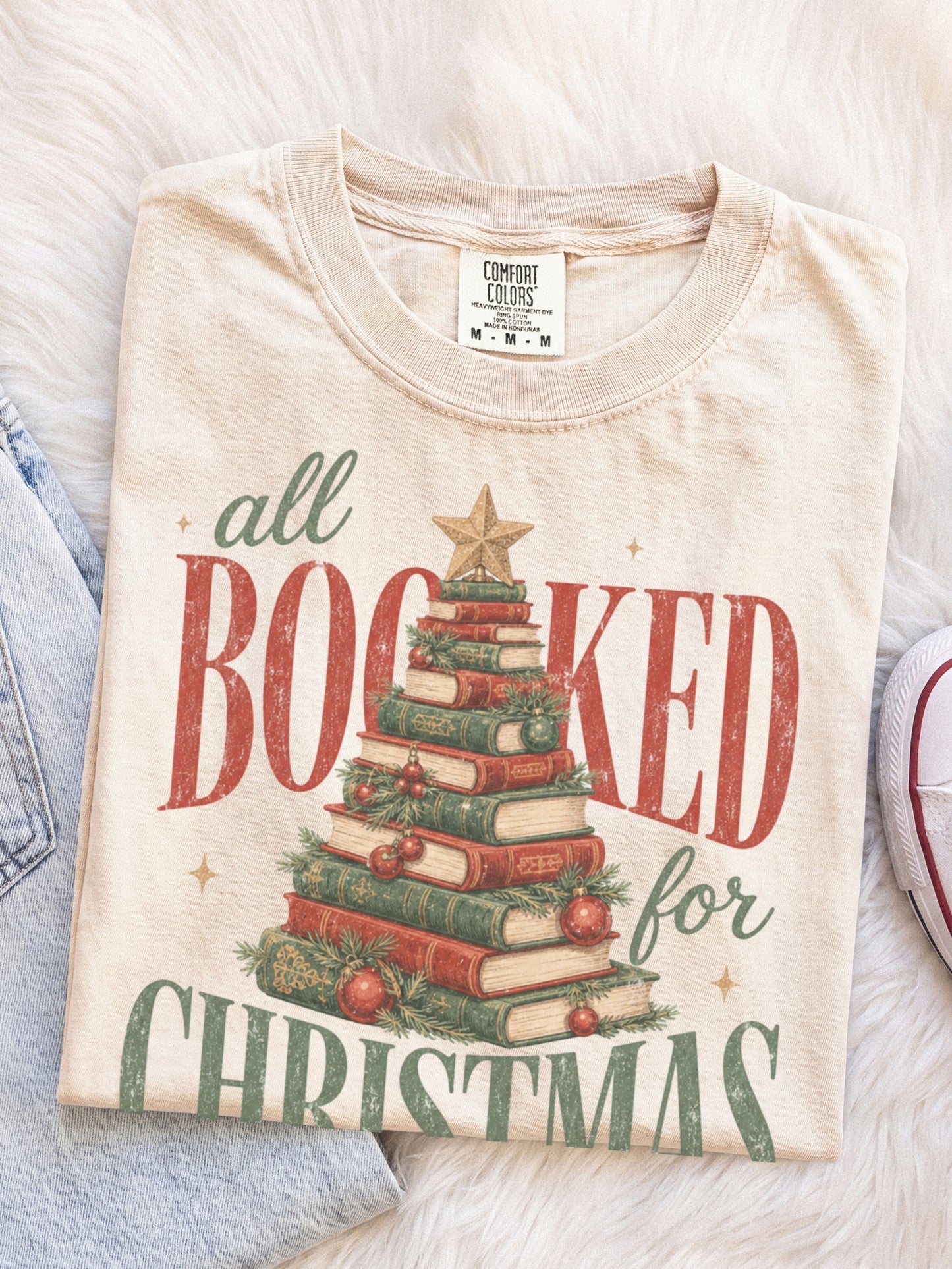 Ivory Comfort Colors shirt featuring a vintage All Booked for Christmas graphic with stacked books arranged as a Christmas tree, evergreen greenery, red ornaments and gold star, cozy Christmas reader shirt and book lover gift
