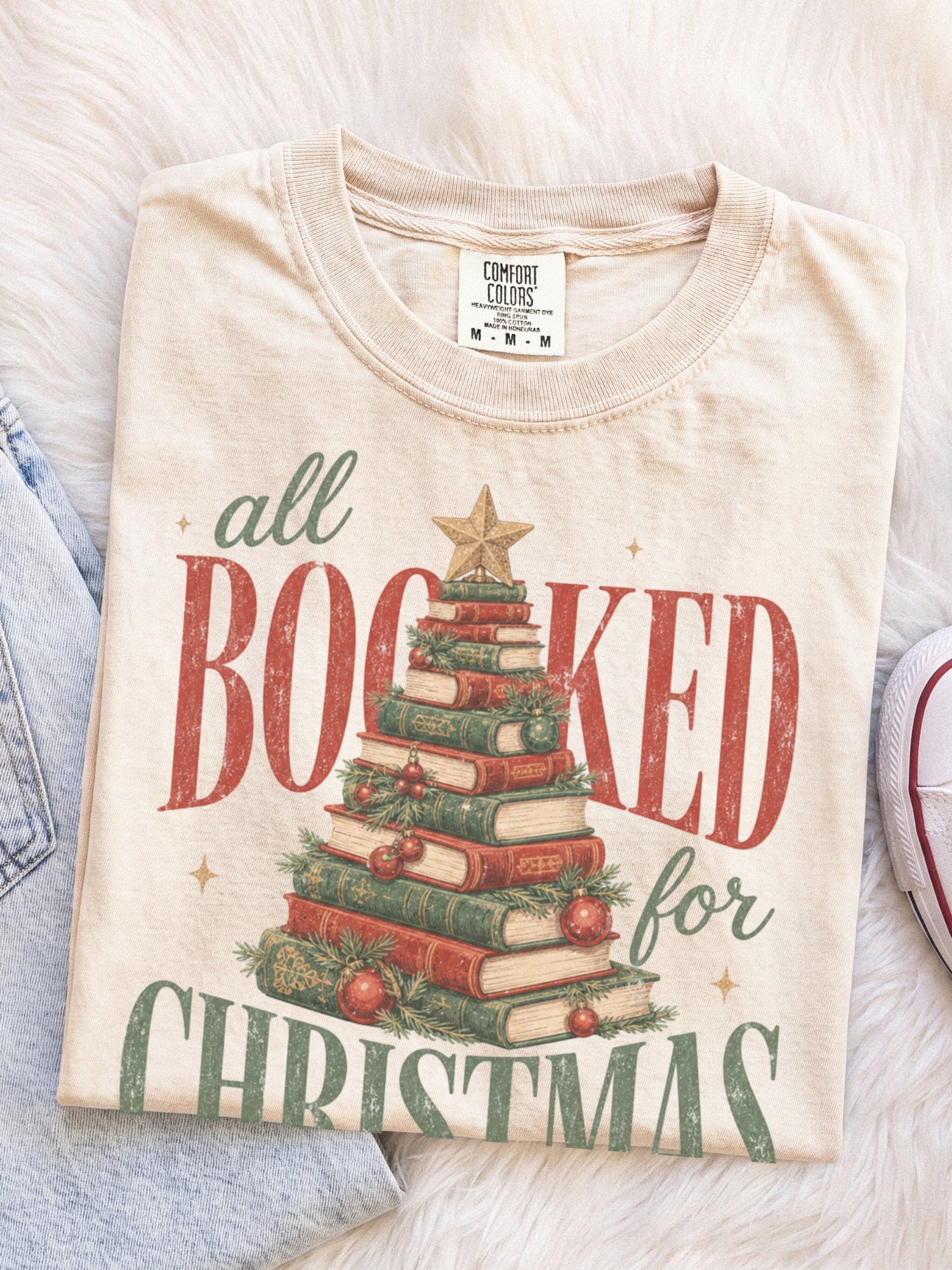 Ivory Comfort Colors shirt featuring a vintage All Booked for Christmas graphic with stacked books arranged as a Christmas tree, evergreen greenery, red ornaments and gold star, cozy Christmas reader shirt and book lover gift