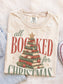 Ivory Comfort Colors shirt featuring a vintage All Booked for Christmas graphic with stacked books arranged as a Christmas tree, evergreen greenery, red ornaments and gold star, cozy Christmas reader shirt and book lover gift