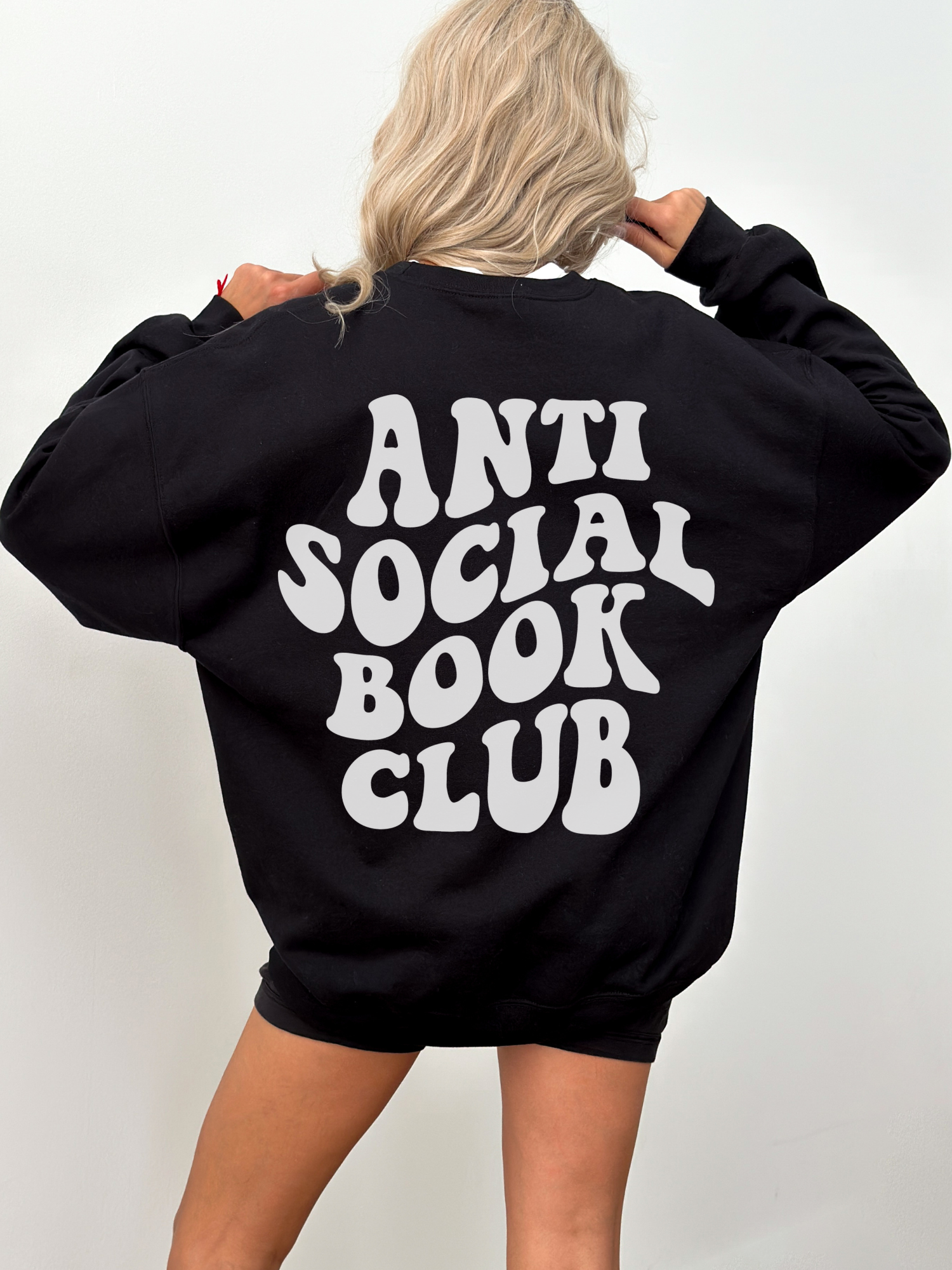 blonde woman facing away wearing oversized black sweatshirt with bold anti social book club text on back