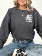woman sitting cross-legged wearing dark heather sweatshirt with anti social book club text and jeans