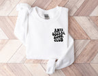 folded white sweatshirt with anti social book club text on wood herringbone background