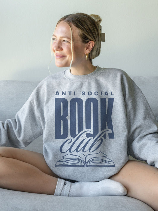 woman sitting on couch wearing ash grey sweatshirt with navy anti social book club text