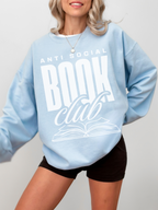 woman in pastel blue sweatshirt that says anti social book club in large white font with open book