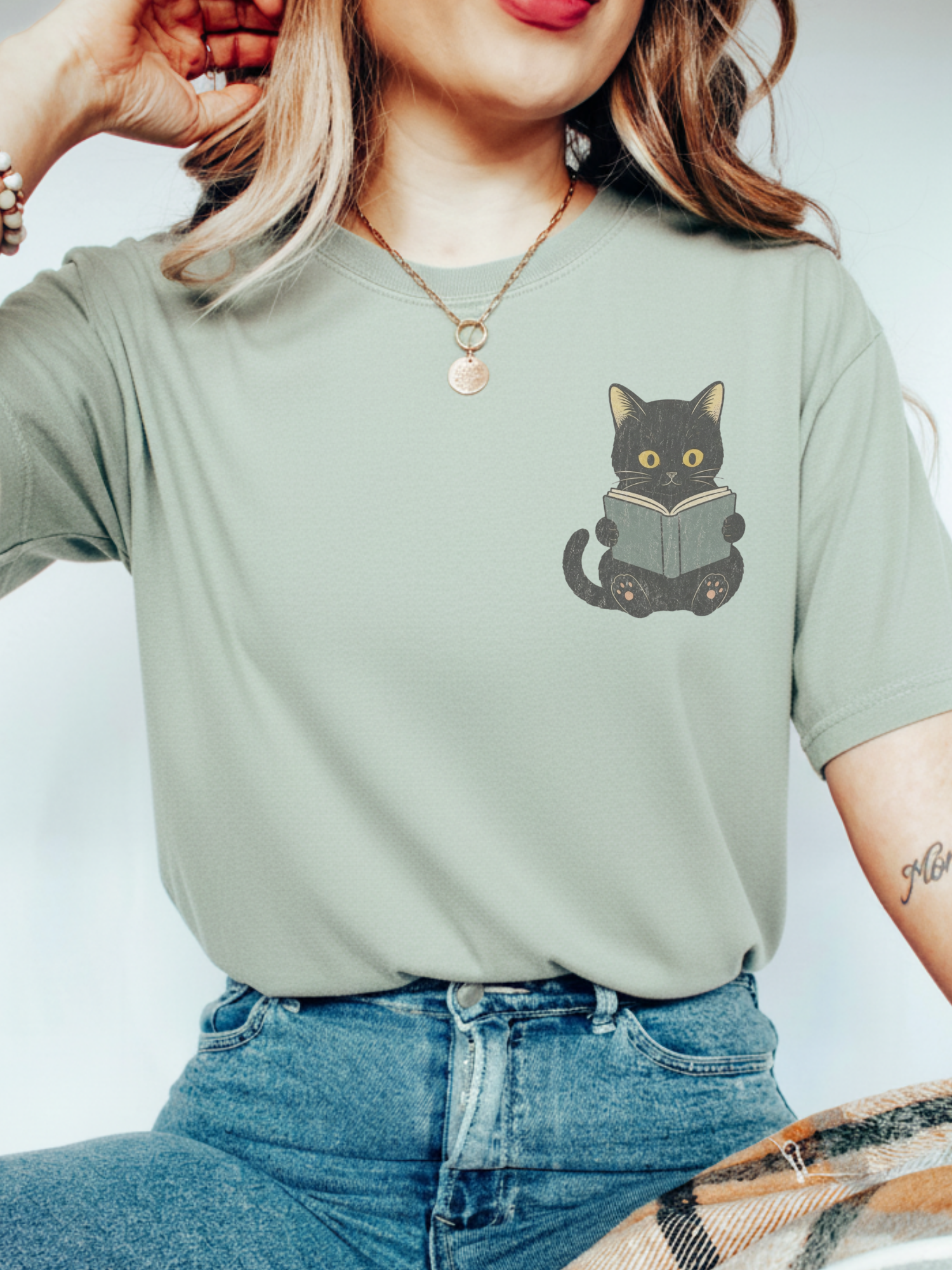 woman wearing a bay Comfort Colors shirt featuring a black cat reading a book pocket design, cute bookish cat shirt for readers, librarians, and cat lovers