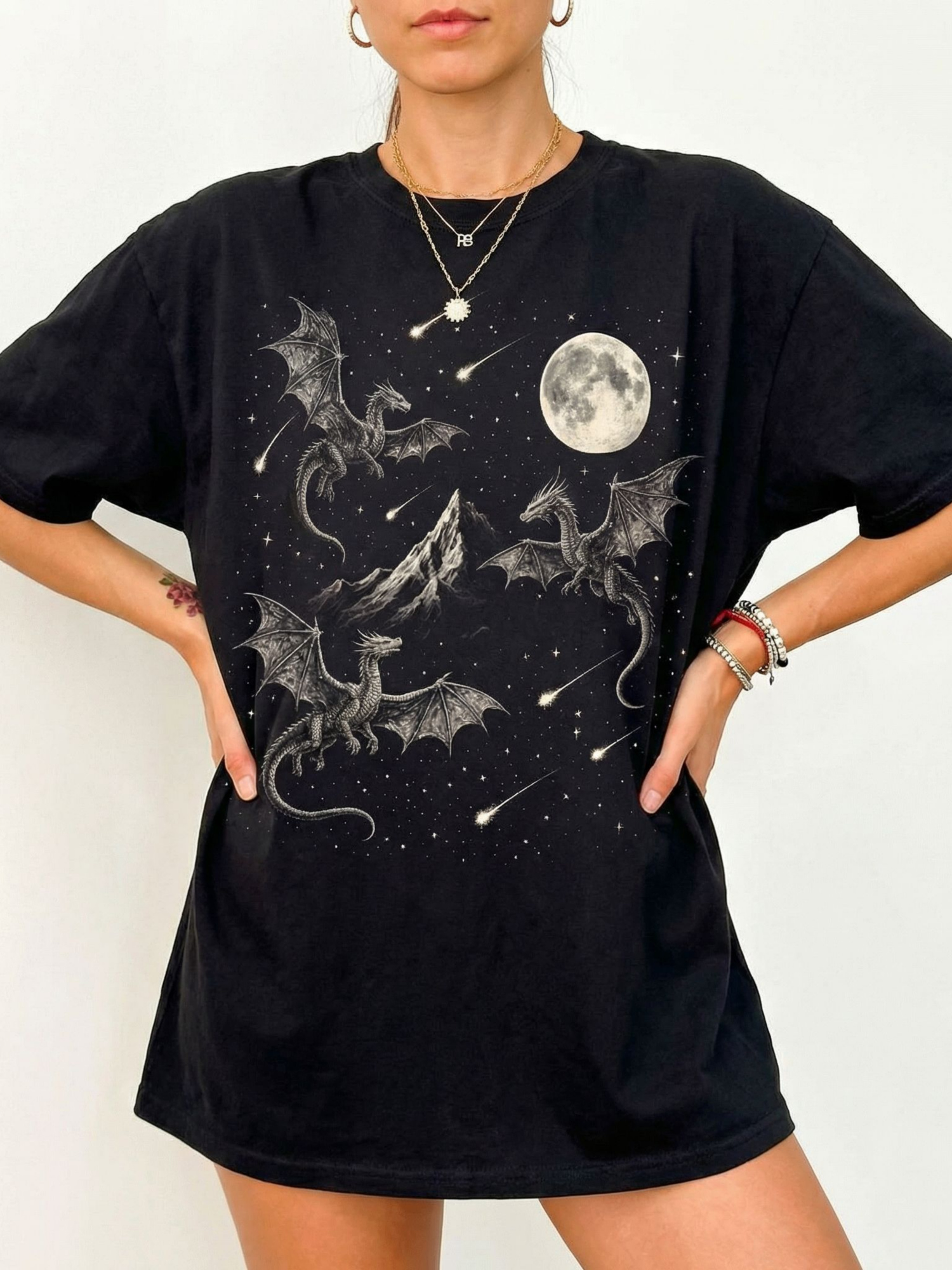 Black oversized t shirt with intricate dragon illustration showing dragons flying around a mountain with a full moon and star filled sky. Fantasy graphic tee for dragon lovers, book readers, and cozy dark academia aesthetic outfits.