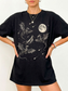 Black oversized t shirt with intricate dragon illustration showing dragons flying around a mountain with a full moon and star filled sky. Fantasy graphic tee for dragon lovers, book readers, and cozy dark academia aesthetic outfits.