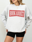 woman wearing an ash grey sweatshirt with red distressed book addict text styled casually with black shorts