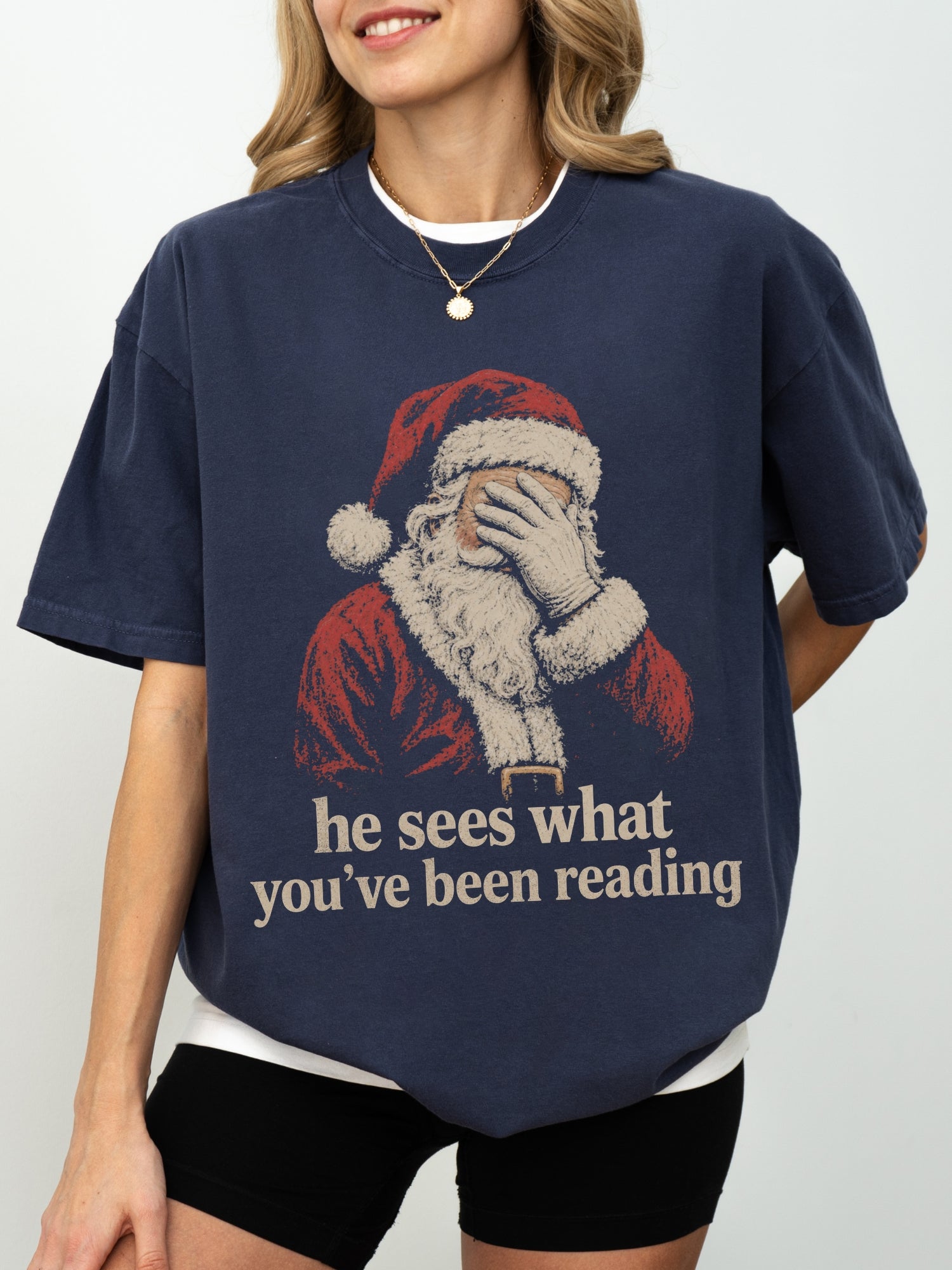 True Navy Comfort Colors shirt modeled with a retro Santa design and he sees what you’ve been reading phrase, a funny bookish Christmas tee for readers
