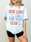 woman wearing a light blue comfort colors t shirt with book lover club text and open book illustration