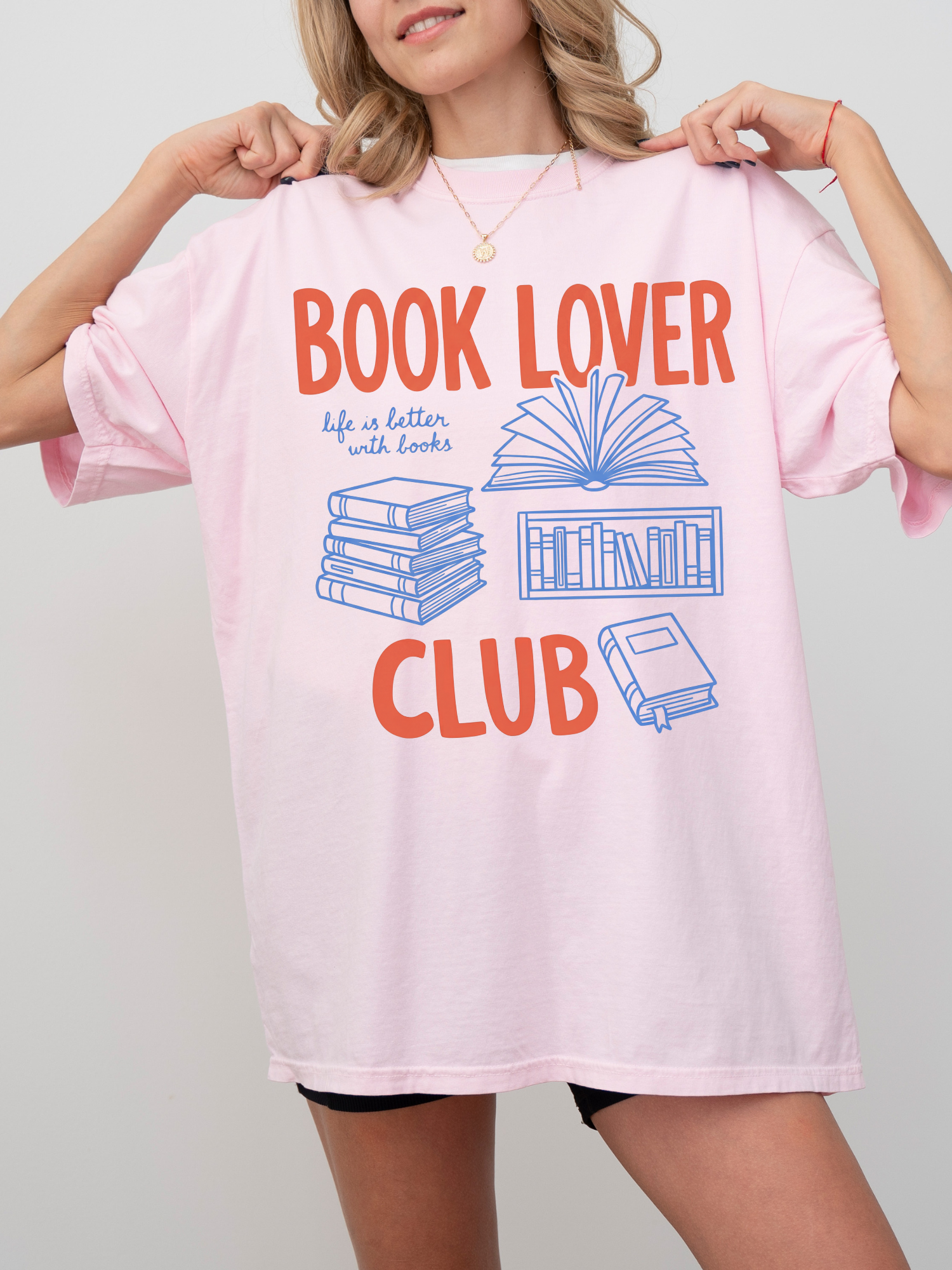 woman wearing a light pink comfort colors t shirt with book lover club graphic and stacked book illustrations