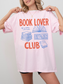 woman wearing a light pink comfort colors t shirt with book lover club graphic and stacked book illustrations