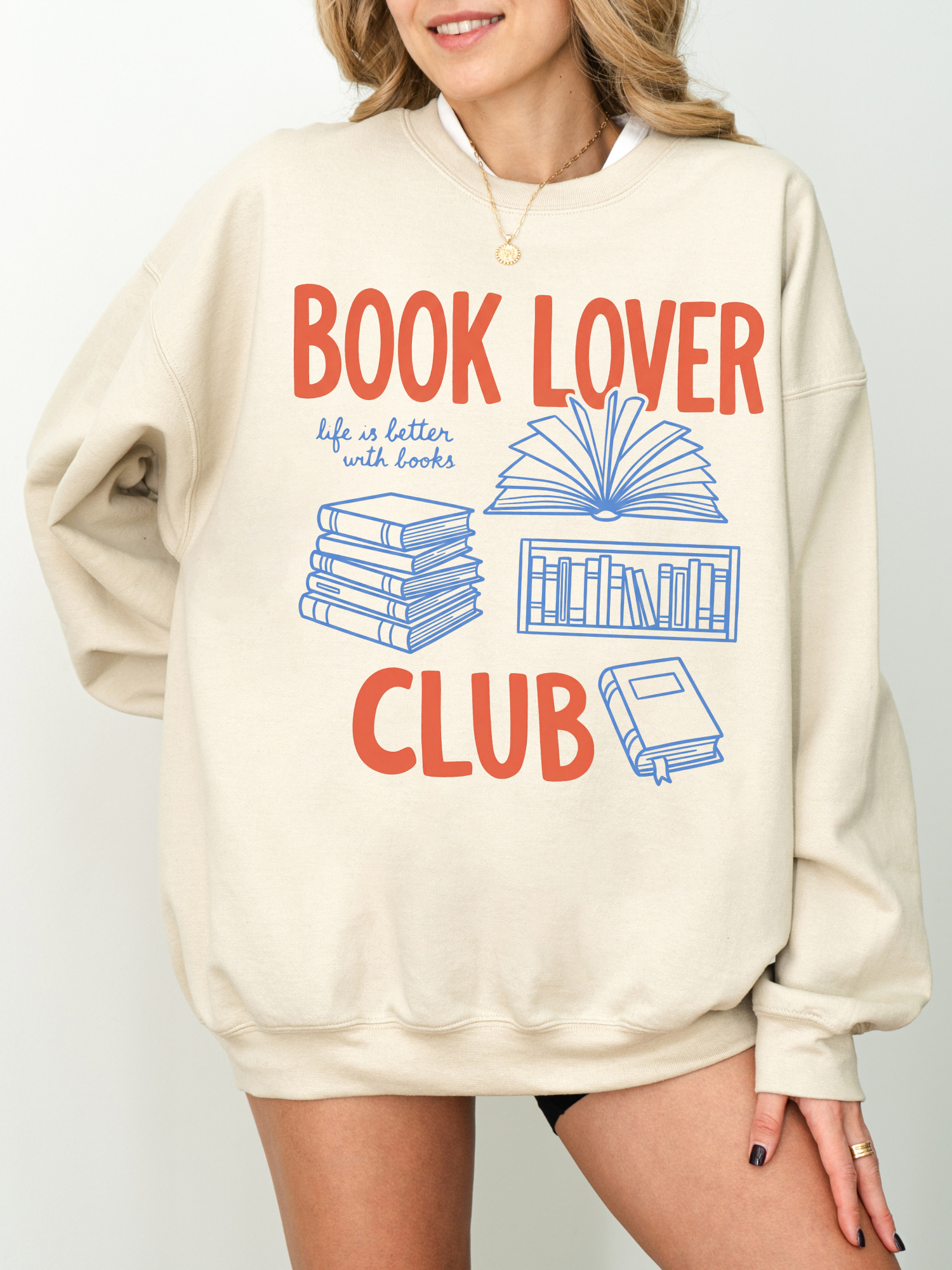 woman wearing a sand colored book lover club sweatshirt with stacked books and open book design
