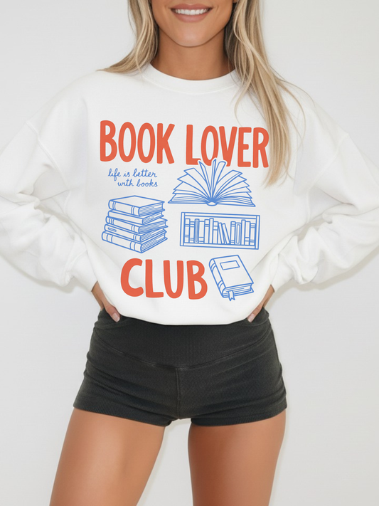 woman wearing a white book lover club sweatshirt with orange and blue book illustrations styled casually
