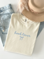 flat lay of cream book lover shirt with bow next to hat and jeans