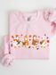 A light pink crewneck sweatshirt featuring a graphic of four cartoon ducks reading books in autumn outfits, surrounded by colorful leaves and acorns. The sweatshirt is neatly folded on a white background with a matching pink fabric bow tied to the upper right corner.