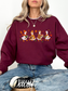 A woman wearing a maroon crewneck sweatshirt with a graphic of four cartoon ducks in autumn colors, paired with blue jeans and a black and white sneaker.