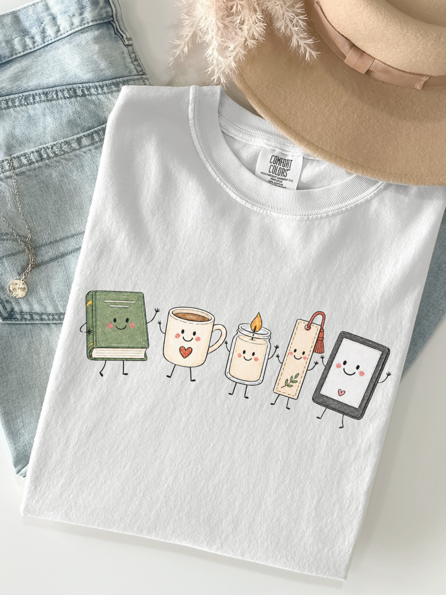 Comfort Colors book lover shirt with cute book, coffee, candle, bookmark and e-reader design styled with jeans and hat in White