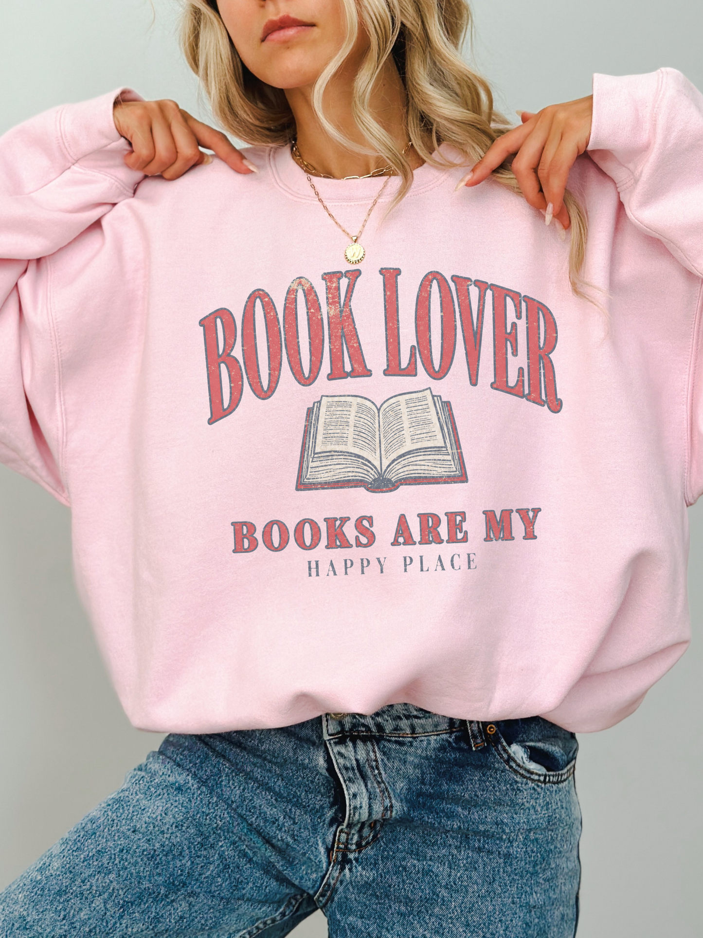 woman wearing a light pink book lover sweatshirt featuring distressed book lover typography and open book graphic