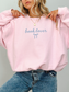 Light pink sweatshirt with “book lover” script and bow, worn with jeans in a soft girl aesthetic