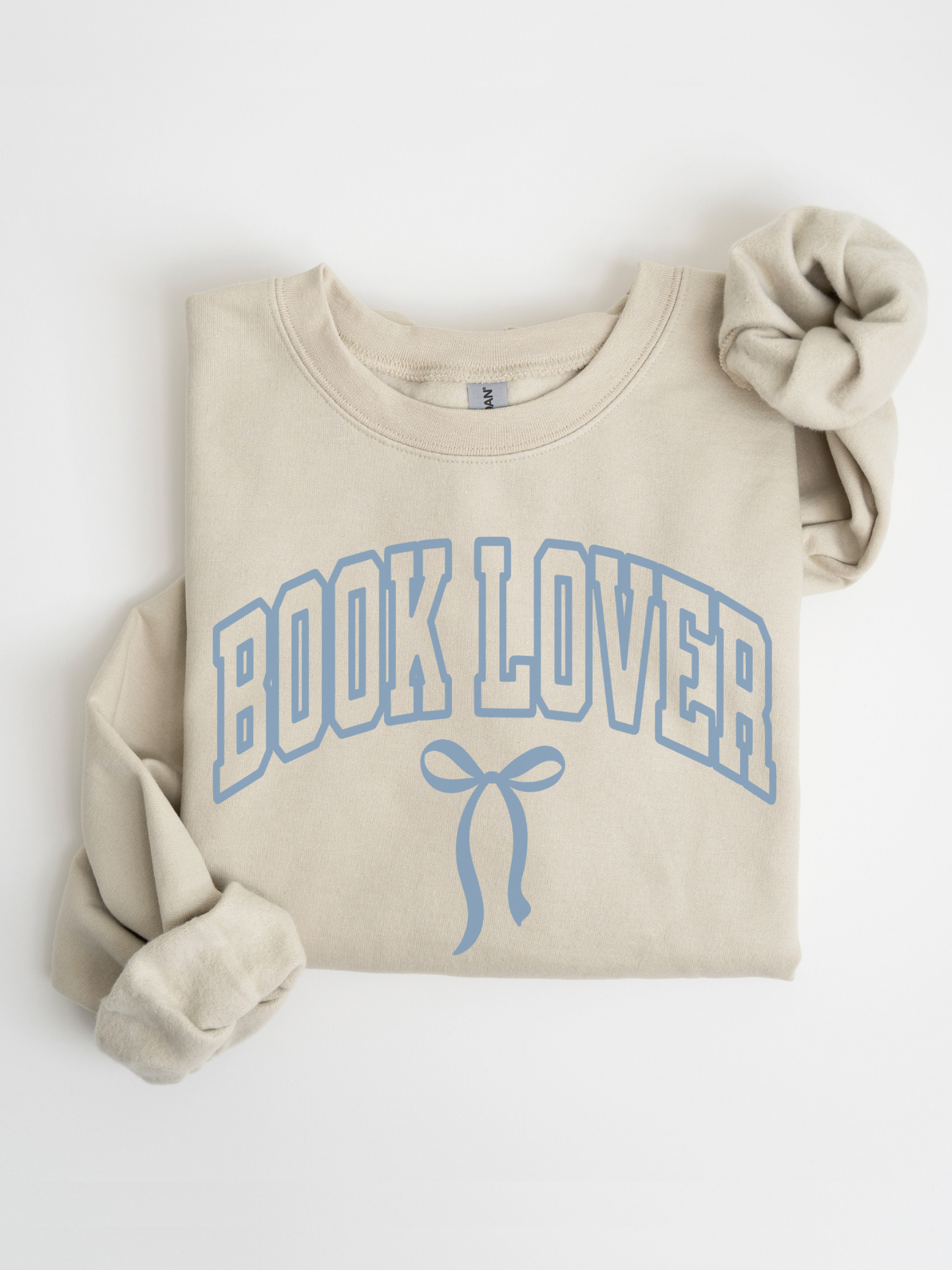 Folded sand-colored Book Lover varsity sweatshirt with blue bow design on white background