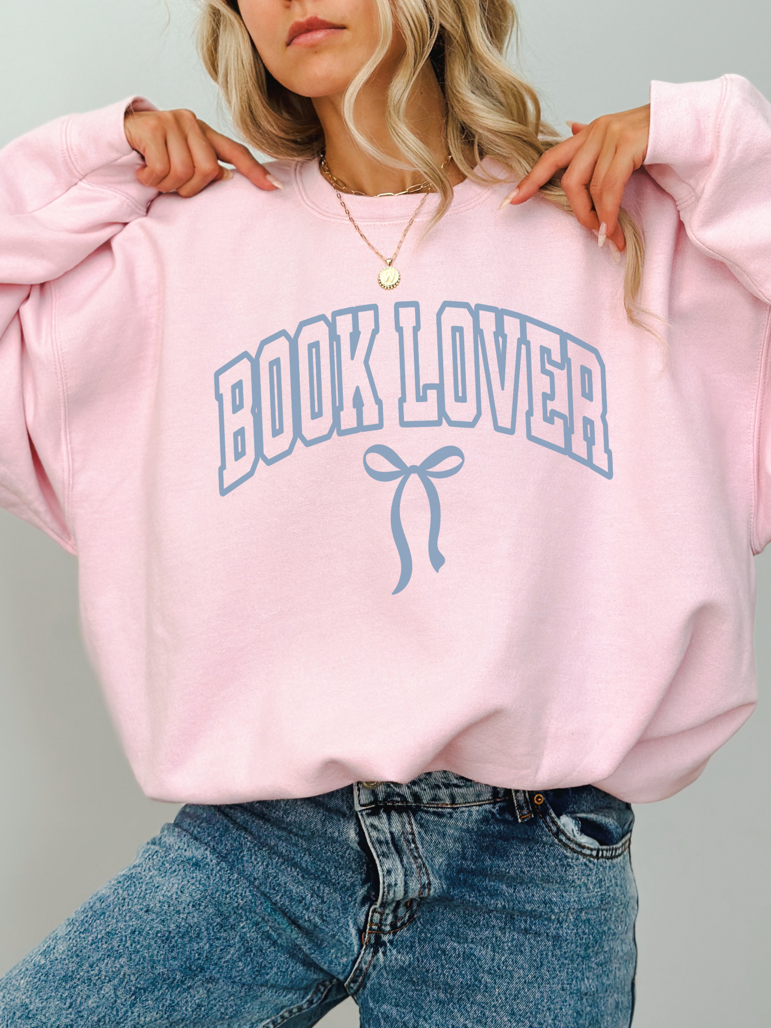 Woman wearing a pastel pink Book Lover sweatshirt with coquette bow print in soft blue, styled with jeans