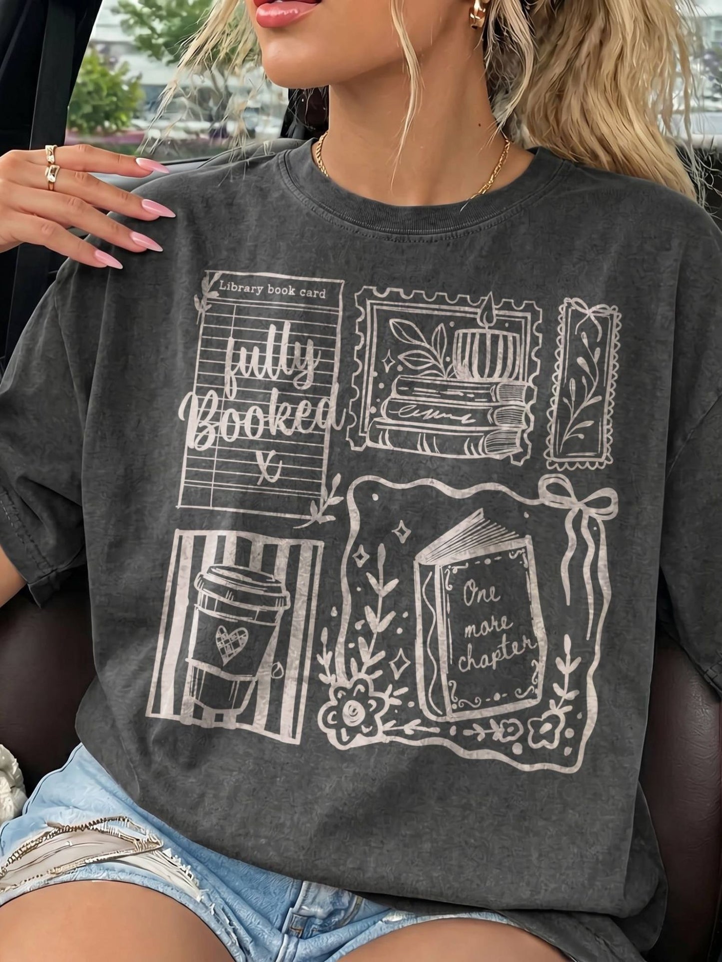A woman wearing a dark gray graphic t-shirt with white illustrations of books, a coffee cup, and text reading 'fully Booked' and 'One more chapter'.