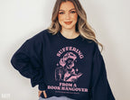 woman wearing navy sweatshirt with pink vintage graphic and text about suffering from a book hangover