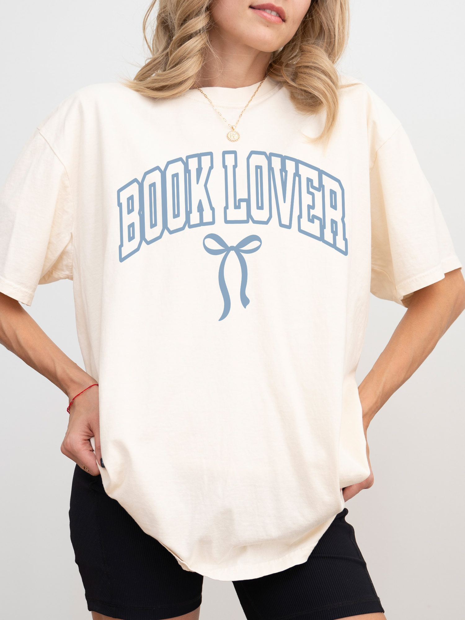 girl wearing a cream ivory t-shirt that says Book Lover with a bow in varsity block font