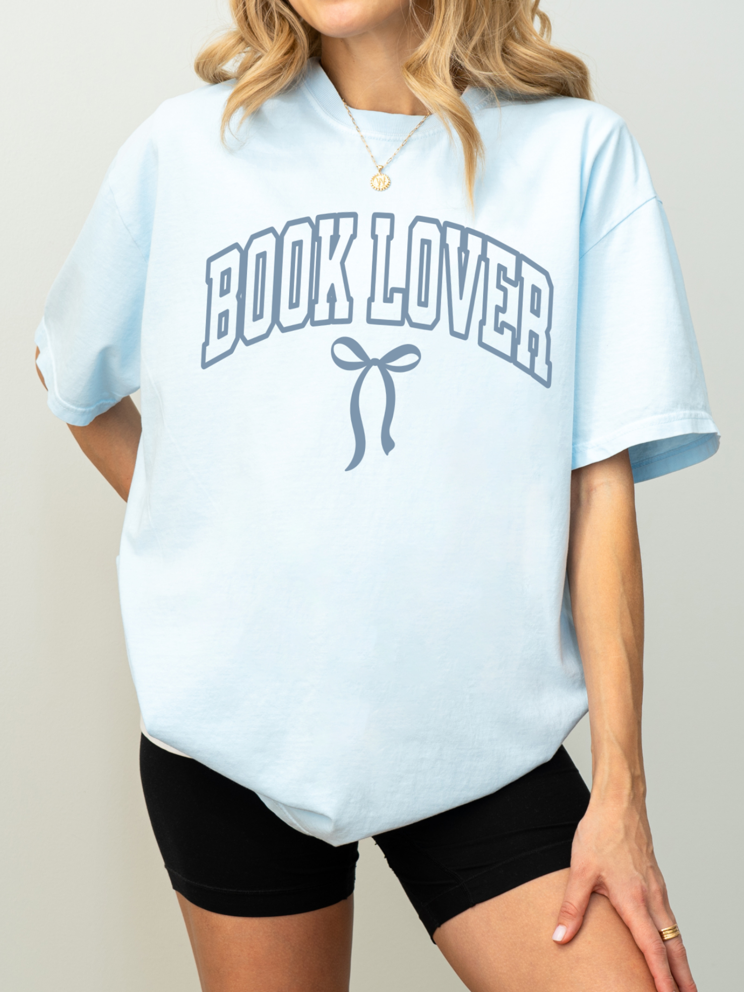 girl wearing a pale blue t-shirt that says Book Lover with a bow in varsity block font