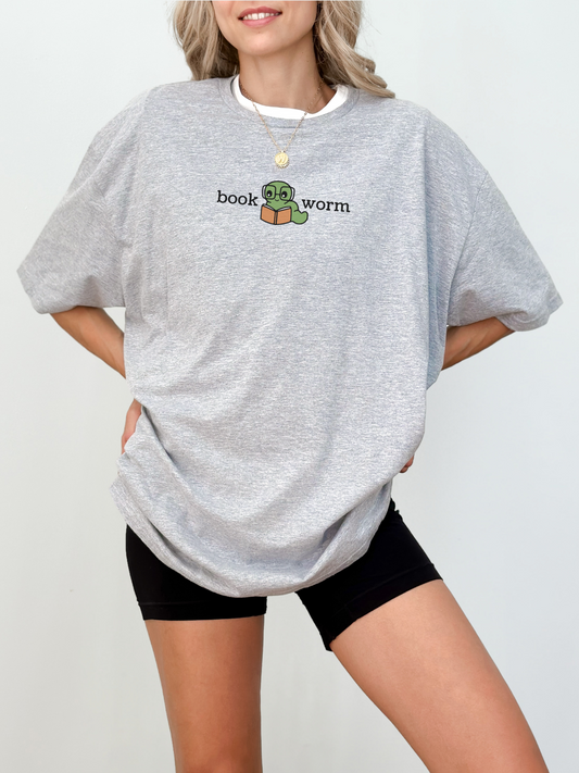 woman wearing an athletic heather t-shirt with a small book worm graphic featuring a green worm and orange book