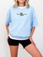 woman wearing a baby blue t-shirt that says book worm with a green cartoon worm and orange book in the center