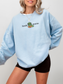 woman wearing a light blue sweatshirt with book worm text and an illustrated green worm with an orange book