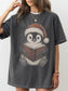 Model wearing a Pepper Comfort Colors bookish shirt with a Christmas penguin in a Santa hat reading a book with holly detail