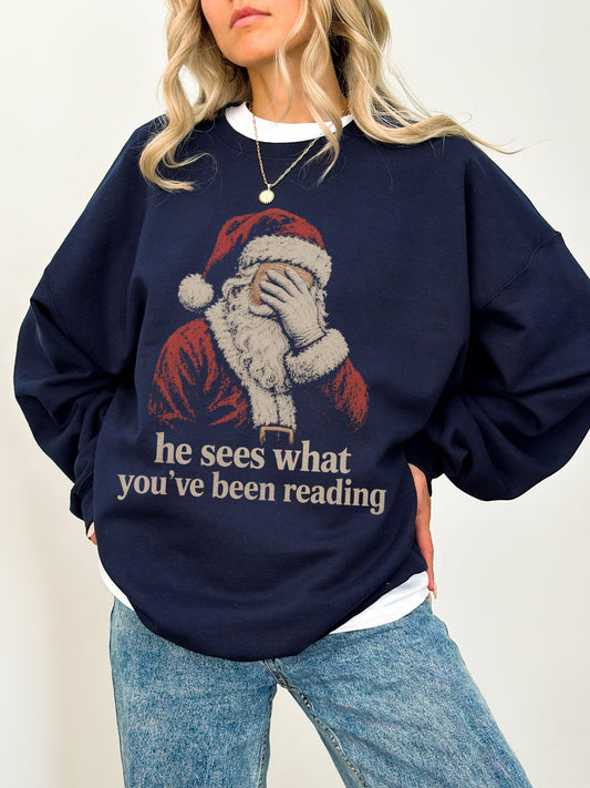 Navy Gildan sweatshirt with vintage Santa covering his eyes and he sees what you’ve been reading phrase, a funny Christmas sweatshirt for book lovers and readers